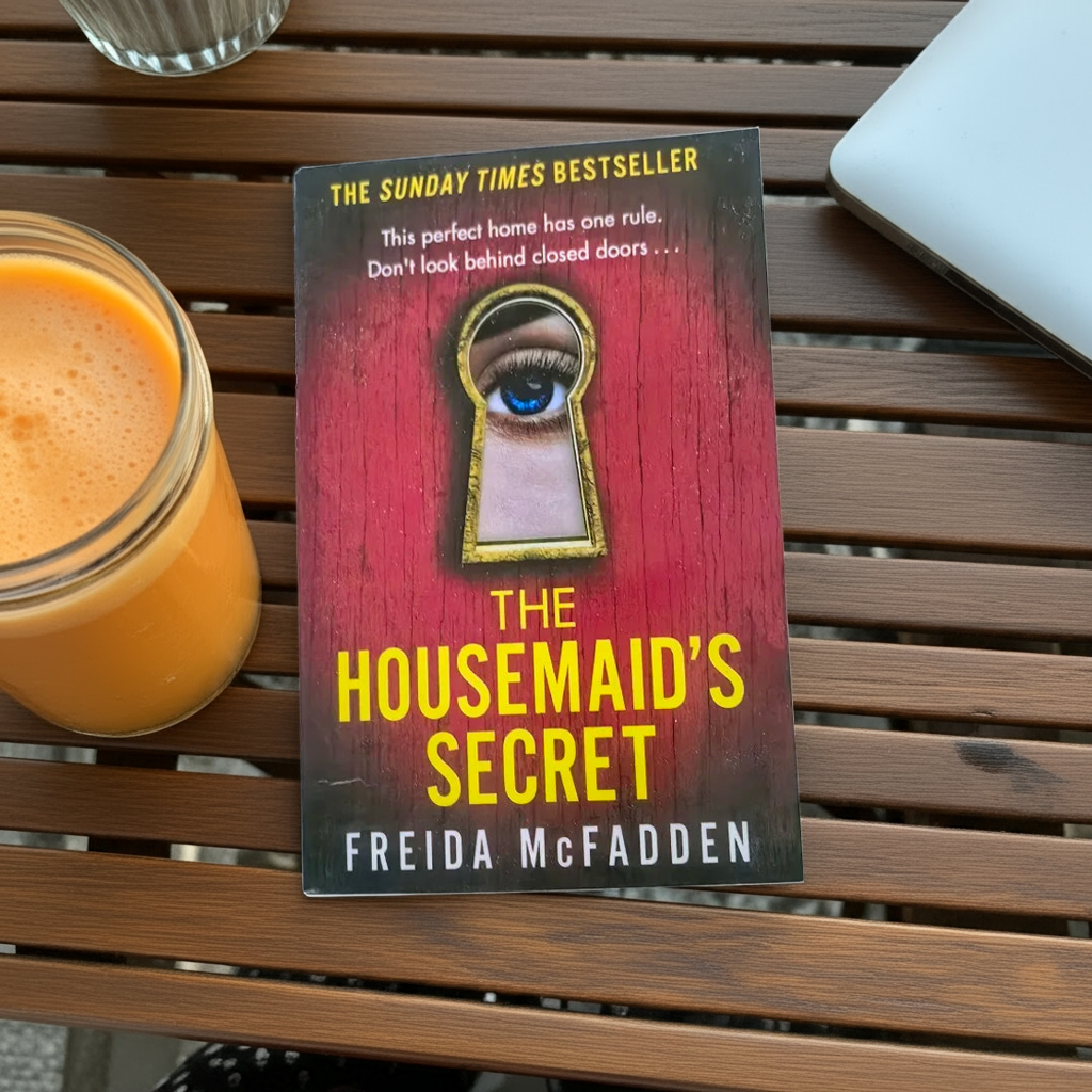 Book cover of 'The Housemaid's Secret' by Freida McFadden  on a table with a juice